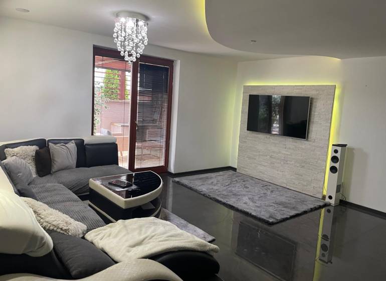 Nappali egy családi házban kanapéval és televízióval a kőburkolatú falon.