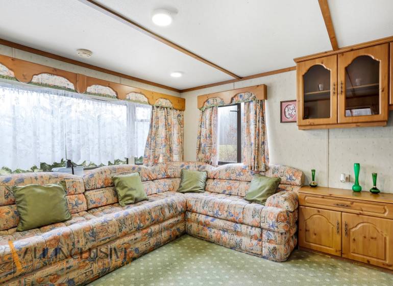 A sarokkanapéval, dekoratív függönyökkel és fa szekrényekkel berendezett házikó belseje.