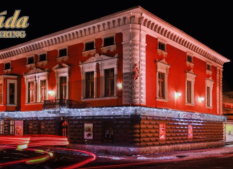 Egy vörös homlokzatú, megvilágított szálloda épülete Poprádon. Szállodák és panziók.