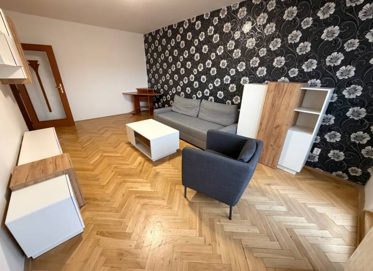 Nappali egy háromszobás lakásban fa mintázatú padlóval, mintás tapétával és bútorokkal.