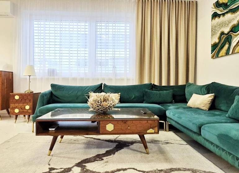 Családi ház zöld árnyalatú kanapéval, fa bútorokkal és művészettel a falon.