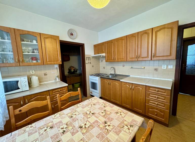 Konyha fa szekrényekkel és étkezőasztallal, amely alkalmas egy háromszobás lakáshoz.