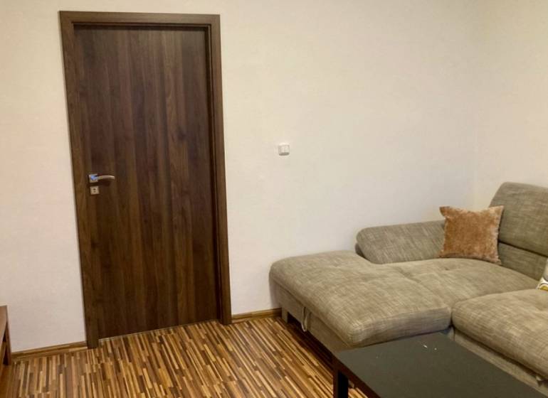 Nappali kanapéval, fa dekor padlóval és sötét ajtókkal egy háromszobás lakásban.