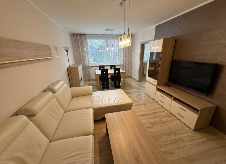 Nappali fa dekor padlóval, nagy kanapéval és étkezőasztallal egy háromszobás lakásban.