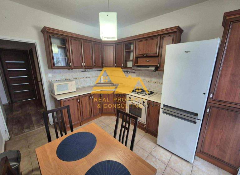 Konyha sötét fa dekorációval, tűzhellyel és hűtőszekrénnyel egy háromszobás lakásban.