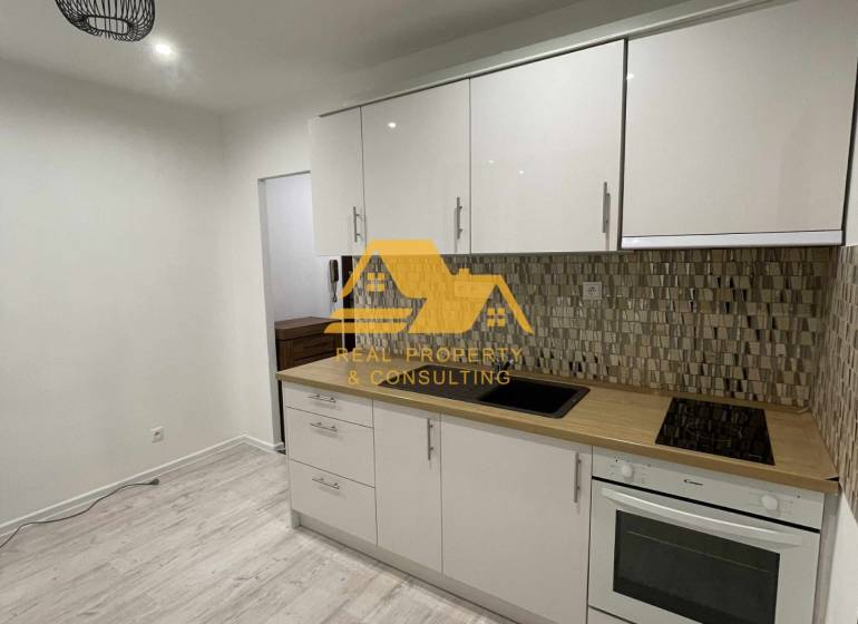 Konyha egy egyszobás lakásban világos konyhabútorral és fa dekorációjú padlóval.