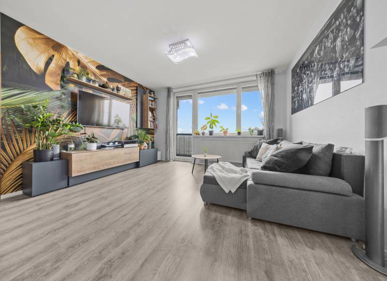 Nappali kényelmes kanapéval, növényi mintás tapétával és fa dekorációjú padlóval.