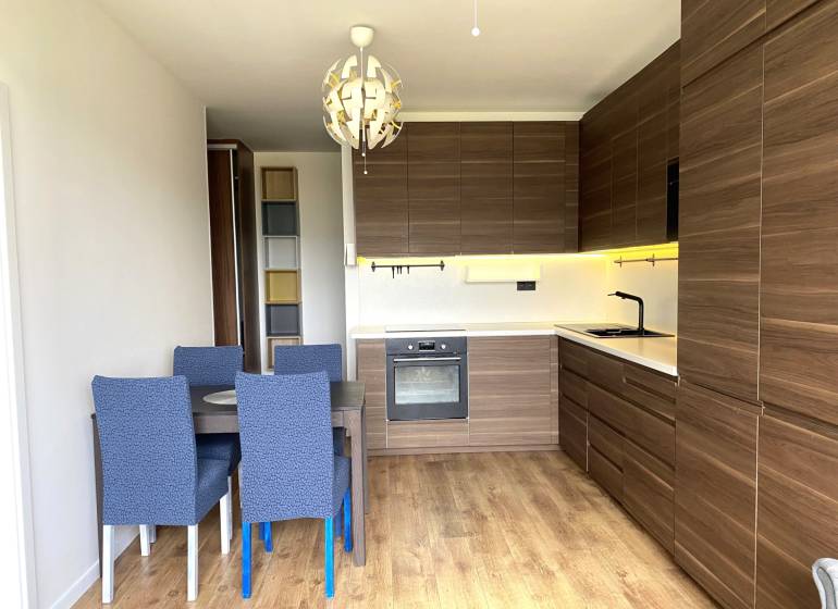 Konyha egy háromszobás lakásban étkezőasztallal, modern világítással és fa dekorációjú padlóval.