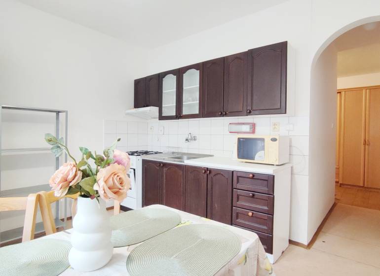 Konyha egy kétszobás lakásban sötét szekrényekkel és dekorációval ellátott étkezőasztallal.