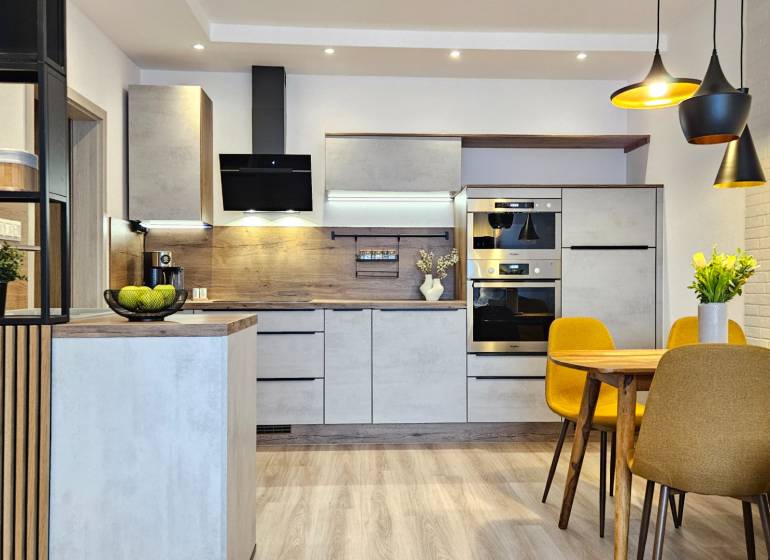 Konyha egy egyszobás lakásban fa dekor padlóval, étkezőasztal és sárga székek.