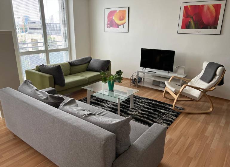Világos nappali kanapékkal, fotellel és televízióval egy kétszobás lakásban.