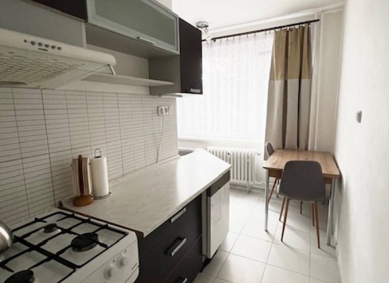 Konyha egy kétszobás lakásban tűzhellyel, sötét bútorokkal és világos csempével.