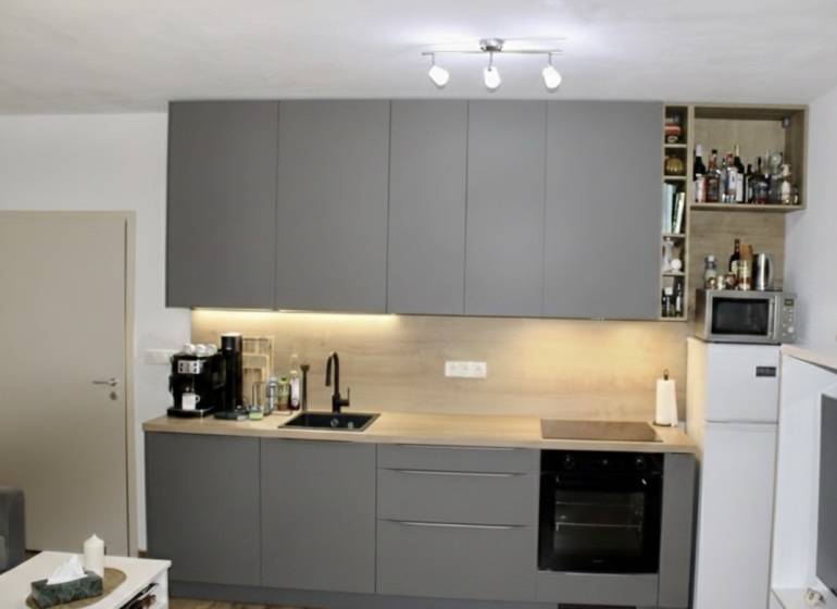 Konyha egy kétszobás lakásban sötétszürke konyhabútorral és háztartási gépekkel.