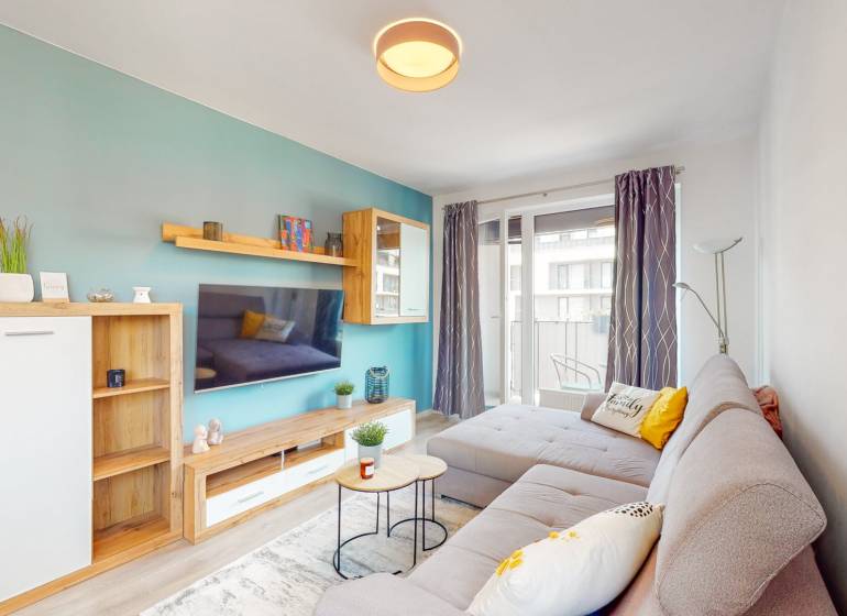 Nappali egy háromszobás lakásban kényelmes kanapéval és erkéllyel, fa dekorációjú padlóval.