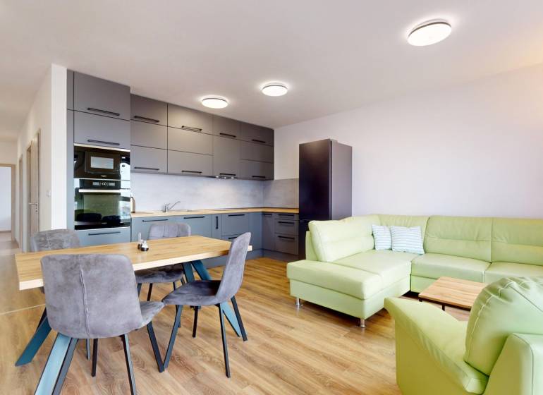 Konyha nappalival a háromszobás lakásban, zöld kanapé, fa dekorú padló.