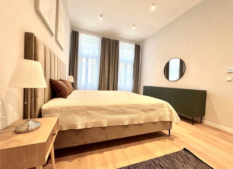 Hálószoba egy kétszobás lakásban nagy ággyal, lámpával és fa dekorációjú padlóval.