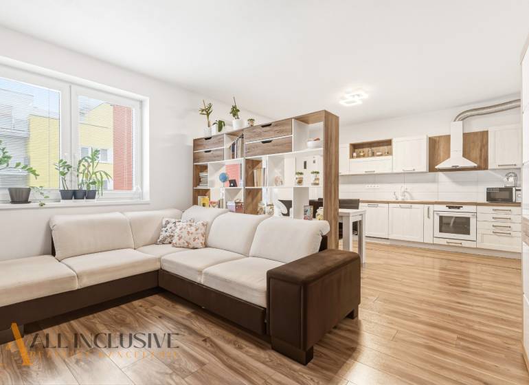 Nappali egy kétszobás lakásban nagy kanapéval és konyhával, fa dekorációjú padlóval.