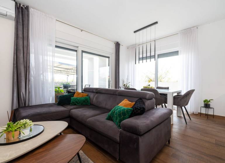 Nappali a nyaraló apartmanban kanapéval, fa hatású padlóval és étkezőasztallal.