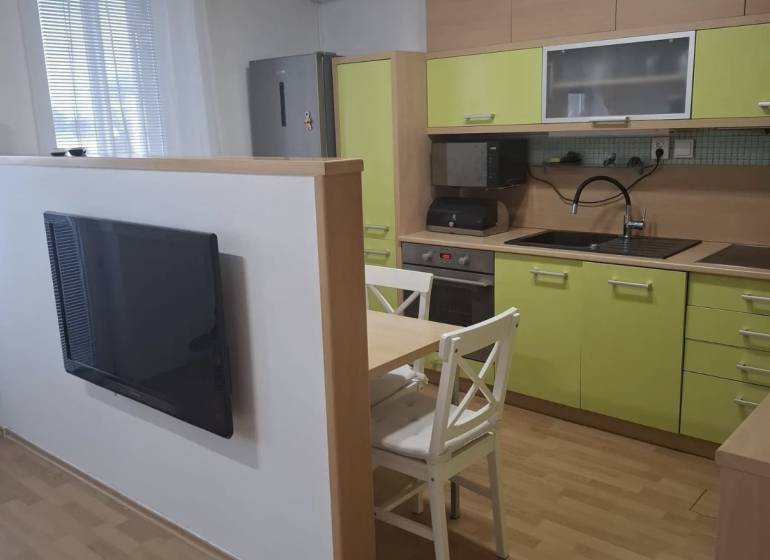 Konyha egy kétszobás lakásban zöld szekrényekkel, televízióval és egy asztallal két székkel.