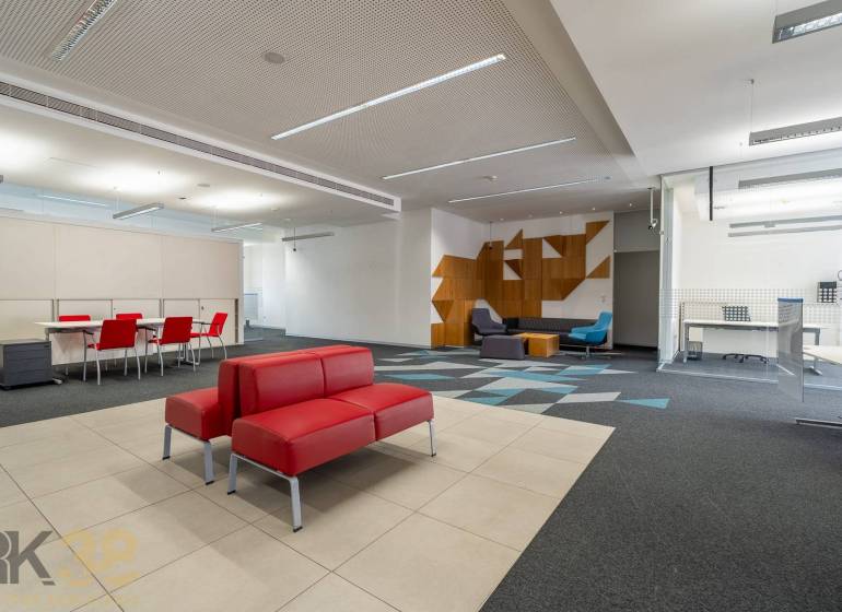 Irodák piros kanapékkal, konferenciaasztallal, mintás szőnyeggel és fa dekorációkkal.