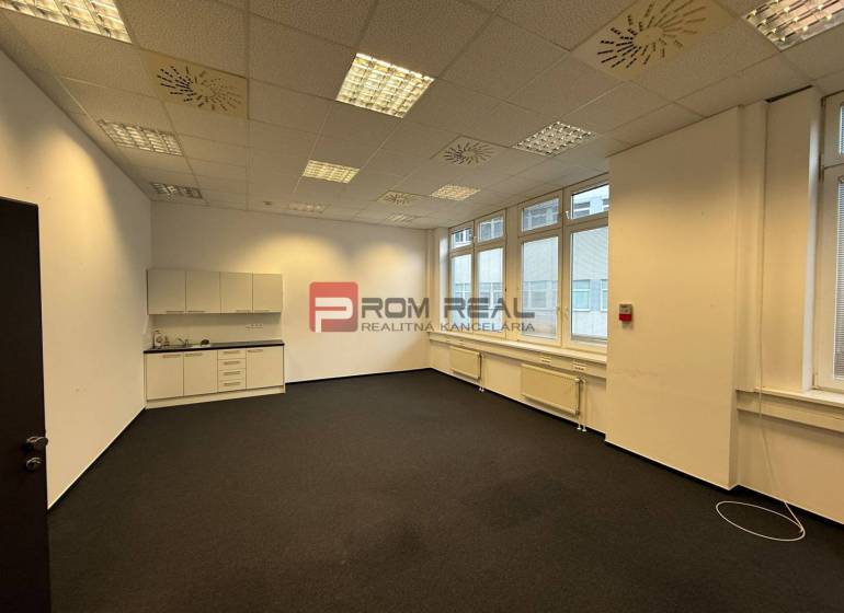 Az irodában fehér szekrények, szőnyegek, mennyezeti lámpák és nagy ablakok vannak.