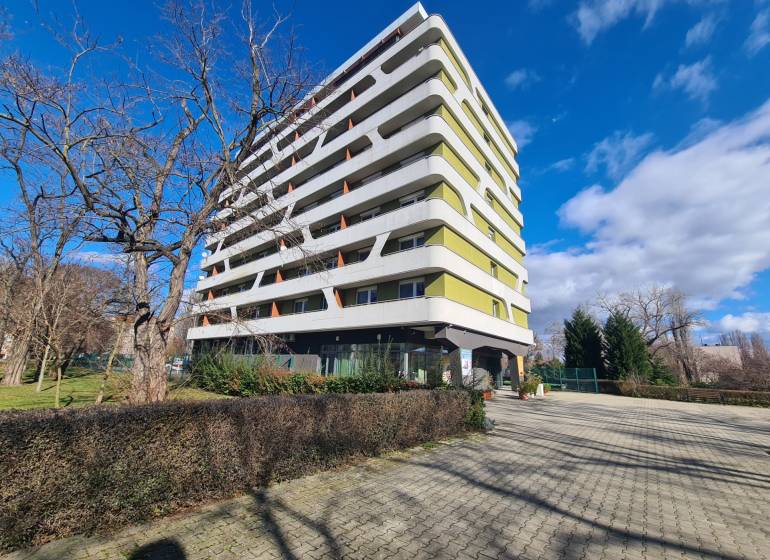 Egy hét emeletes lakóház Komáromban, fákkal körülvéve és burkolt járdával.