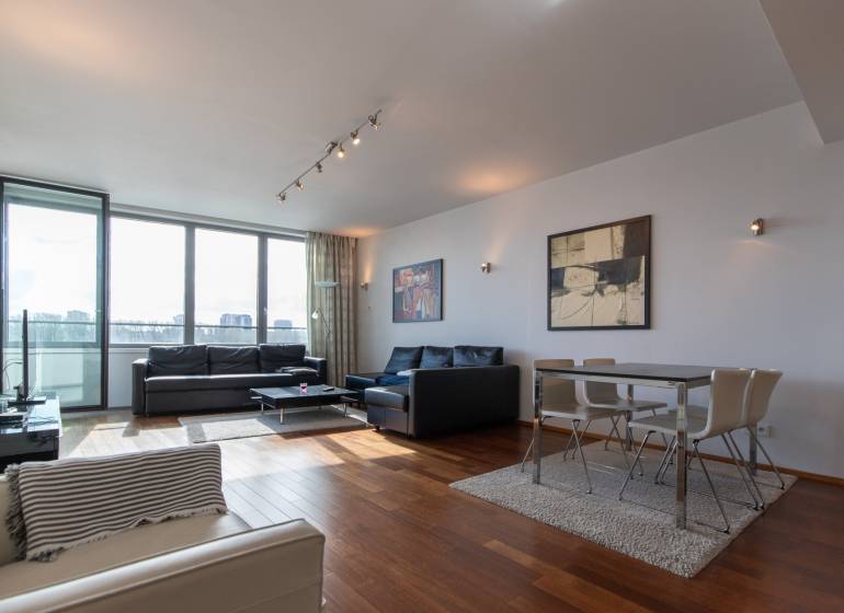 Nappali nagy ablakokkal, fa dekorációjú padlóval, kényelmes bútorokkal és étkező sarokkal.