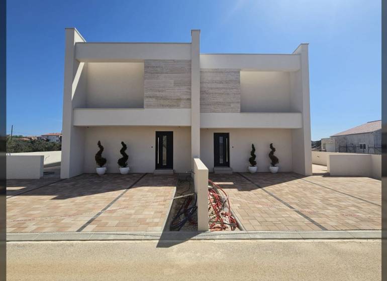 Családi ház a Mulo utcában, Vrsi-ben, burkolt sétánnyal és dekoratív növényekkel.