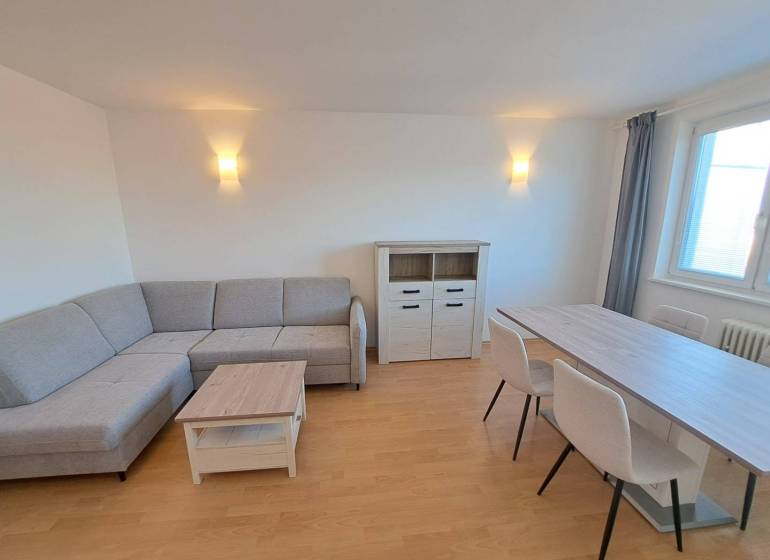 Nappali egy négy szobás lakásban sarokkanapéval és étkezőasztallal.