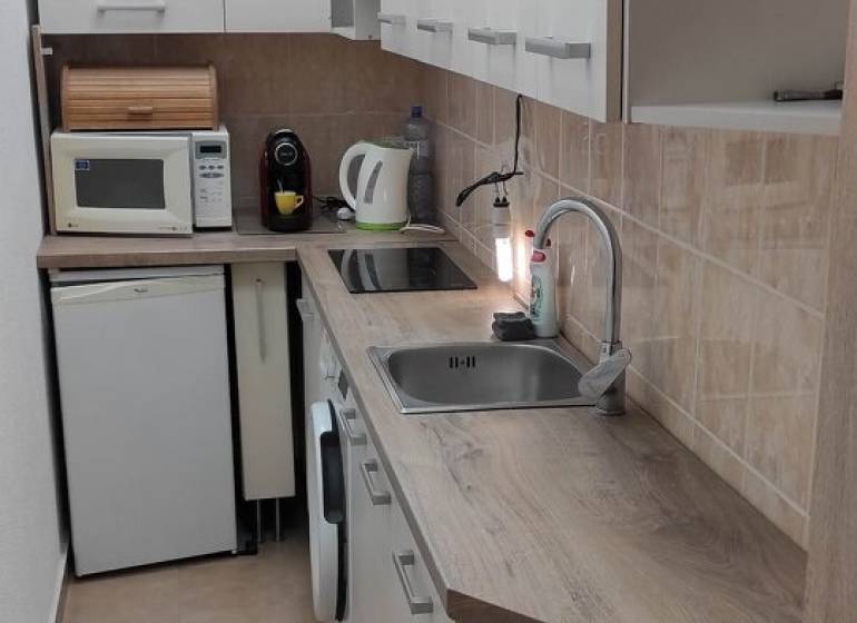 Keskeny konyha egy egyszobás lakásban, konyhapulttal, készülékekkel és tárolószekrényekkel.