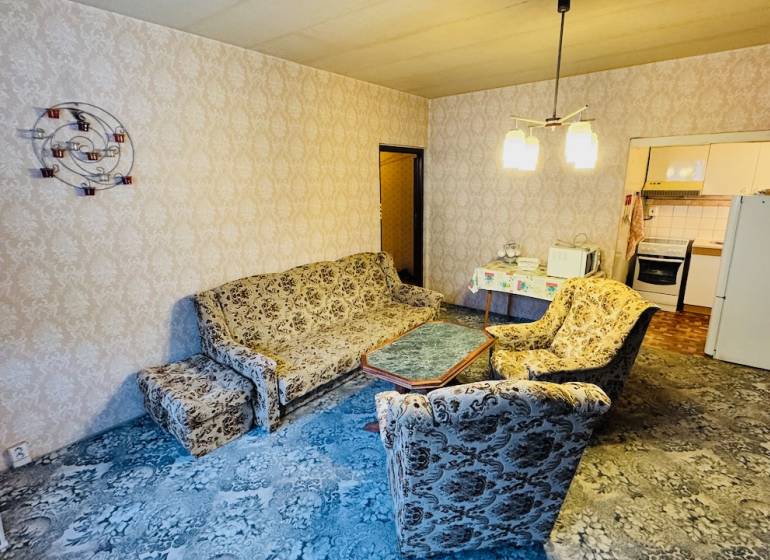 Nappali retro ülőgarnitúrával, mintás szőnyeggel, bejárat a konyhába egy kétszobás lakásban.