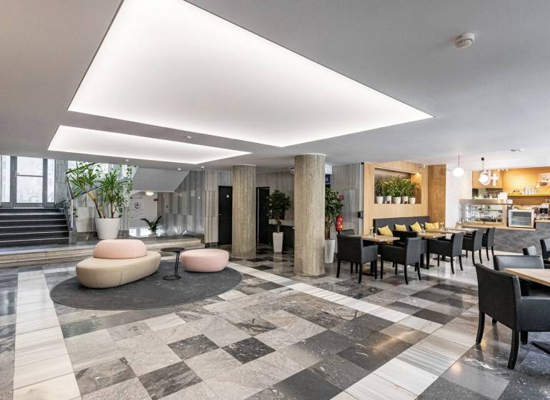 Irodák fekete-fehér padlóval, oszlopokkal, ülőhelyekkel és kávézóval a belső térben.