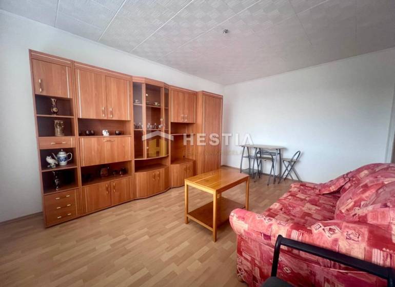 Nappali egy háromszobás lakásban piros kanapéval és fa nappali szekrénnyel.