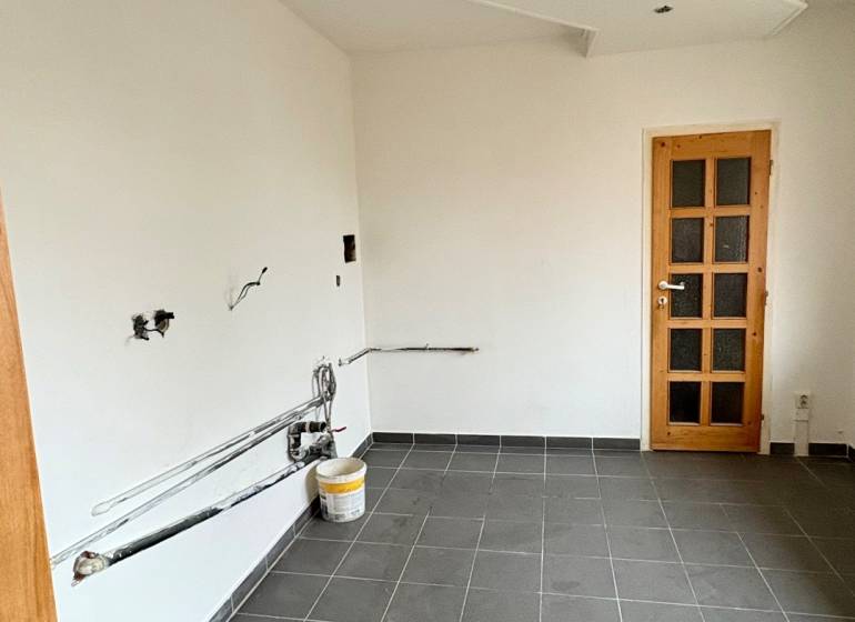 Üres szoba egy kétszobás lakásban, sötét csempézett padló, fehér falak, faajtók.