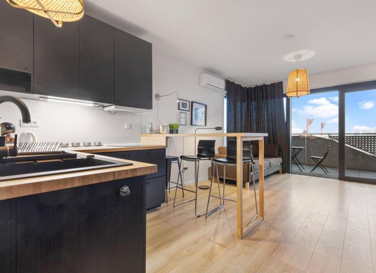 Konyha fekete szekrényekkel, bárpulttal és fa dekorációjú padlóval egy egyszobás lakásban.