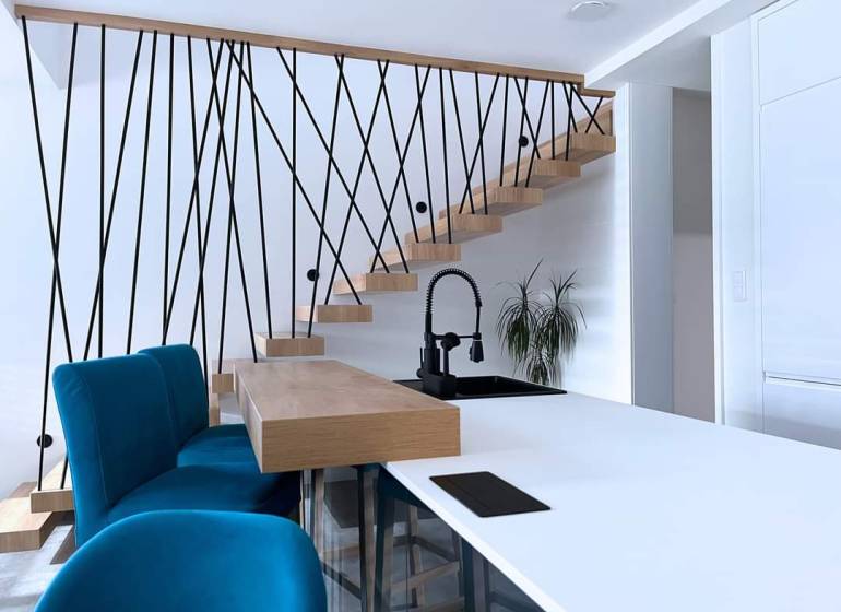 Családi ház belső tere lépcsővel, kék székekkel és konyhapulttal.