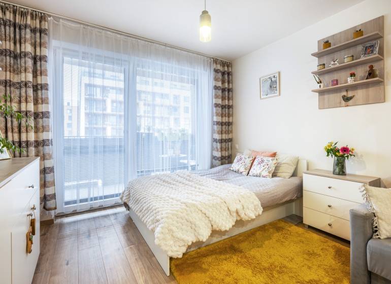 Világos egyszobás lakás ággyal, szőnyeggel és fa dekor padlóval.