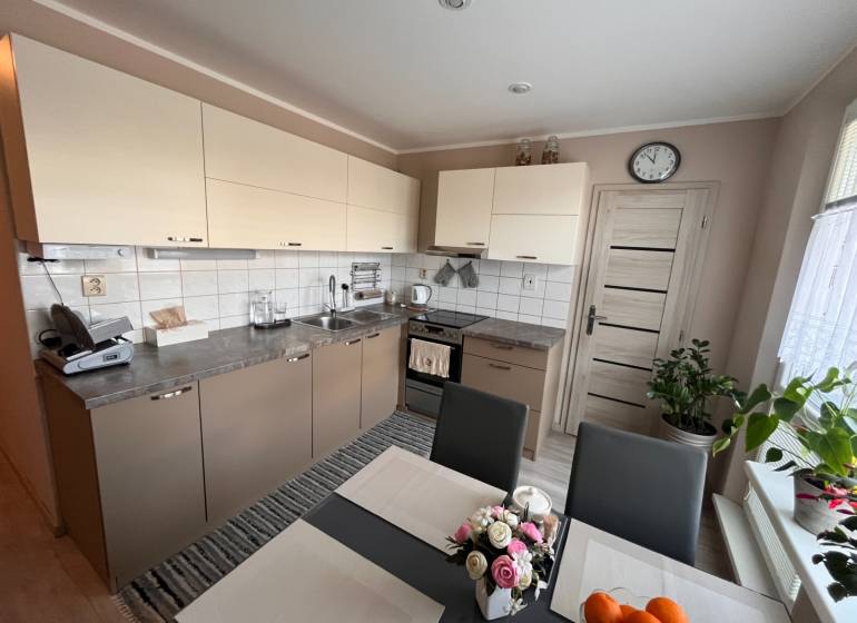 Konyha egy háromszobás lakásban világos szekrényekkel és étkezőasztallal.