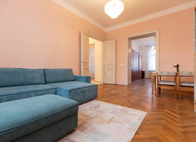 Szoba egy háromszobás lakásban kék kanapéval, fa dekorációjú padlóval és étkező sarokkal.