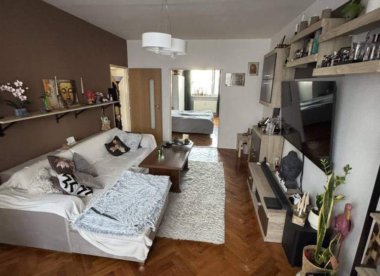 Nappali kanapéval, asztallal és fa dekorációjú padlóval egy háromszobás lakásban.