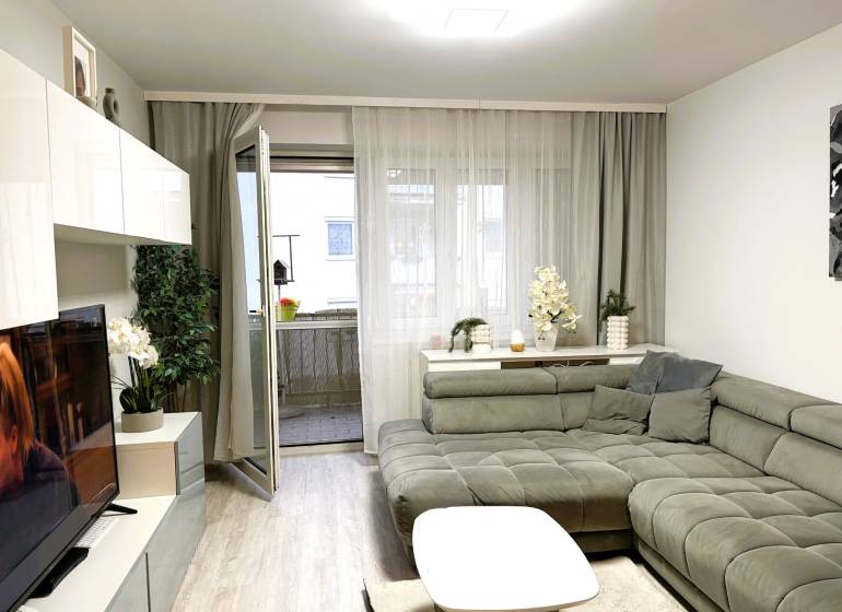 Nappali egy háromszobás lakásban kényelmes kanapésarokkal és fa dekorációjú padlóval.