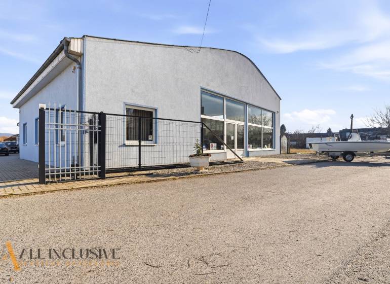 Üzlethelyiség Párkányban szürke homlokzattal, parkolóval és előtetővel.