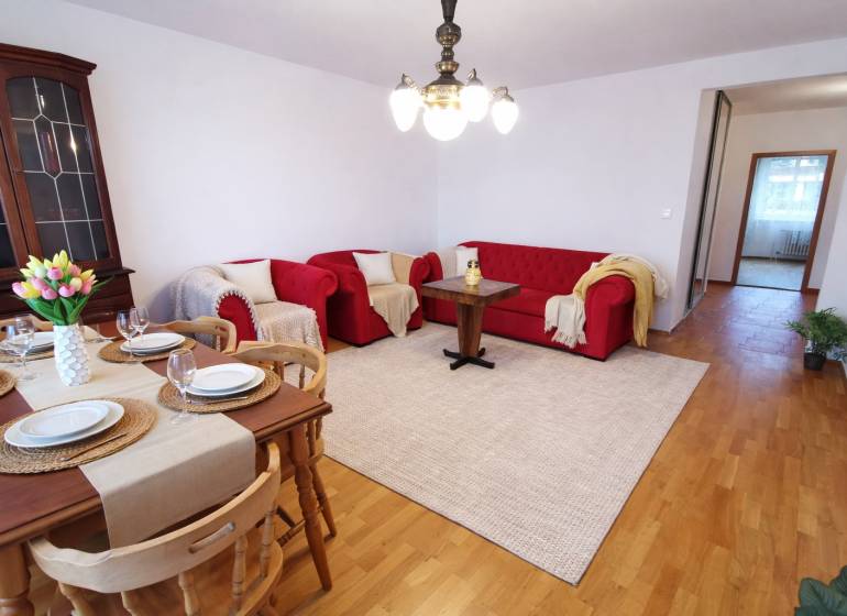 Nappali egy négy szobás lakásban piros kanapékkal, étkezőasztallal és fa mintázatú padlóval.