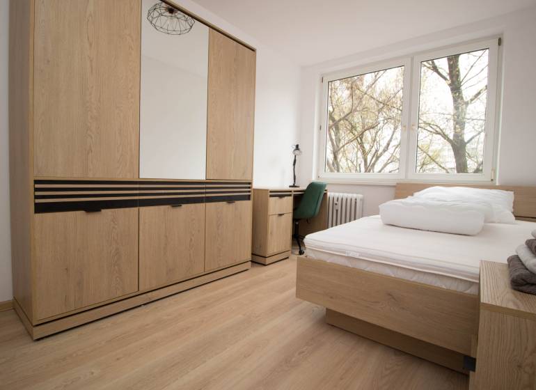 Hálószoba egy háromszobás lakásban ággyal, szekrénnyel és fa dekorációjú padlóval.