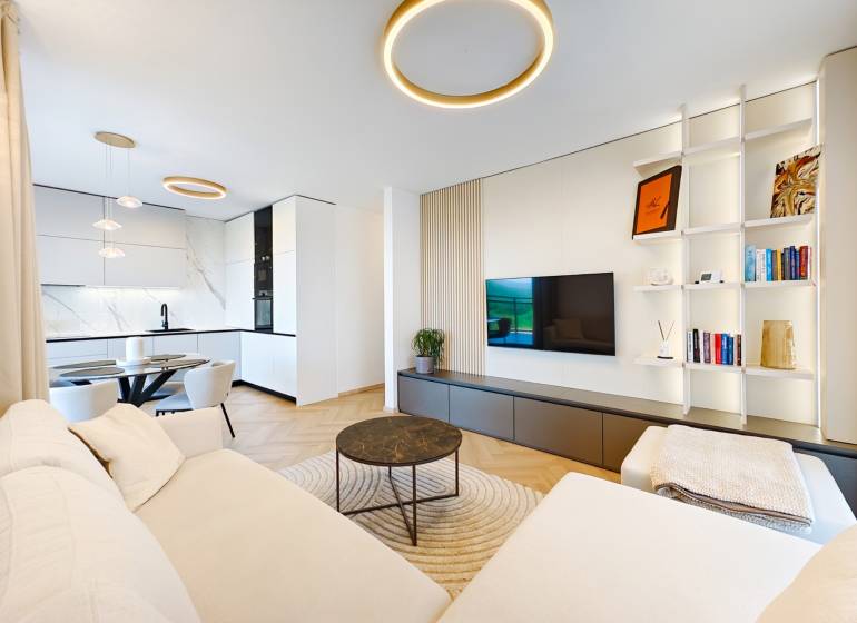 Nappali egy kétszobás lakásban kanapéval, konyhával és fa dekoros padlóval.