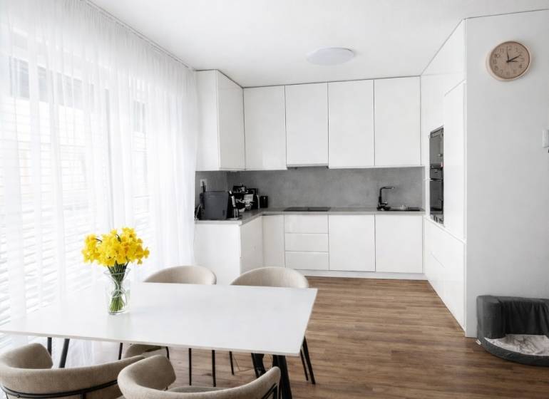 Étkezőasztal székekkel és konyha egy háromszobás lakásban, fa dekorációjú padlóval.