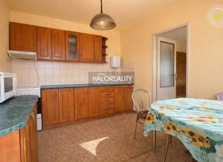 Konyha családi házban beépített szekrényekkel és virágos terítővel ellátott asztallal.