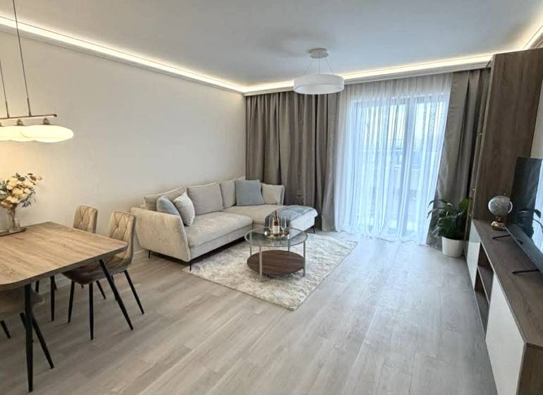 Nappali egy kétszobás lakásban, fa mintázatú padlóval, kanapéval és étkezőasztallal.