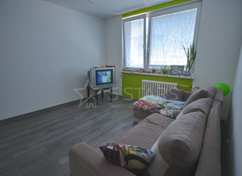 Nappali egy egyszobás lakásban fa mintás padlóval és régebbi televízióval.