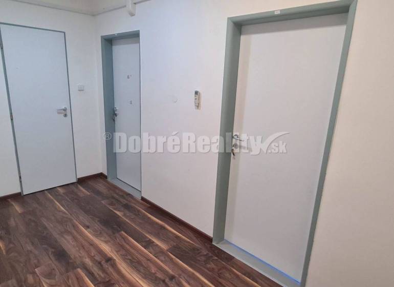 Irodák fehér falakkal, két ajtóval és fa mintázatú padlóval.